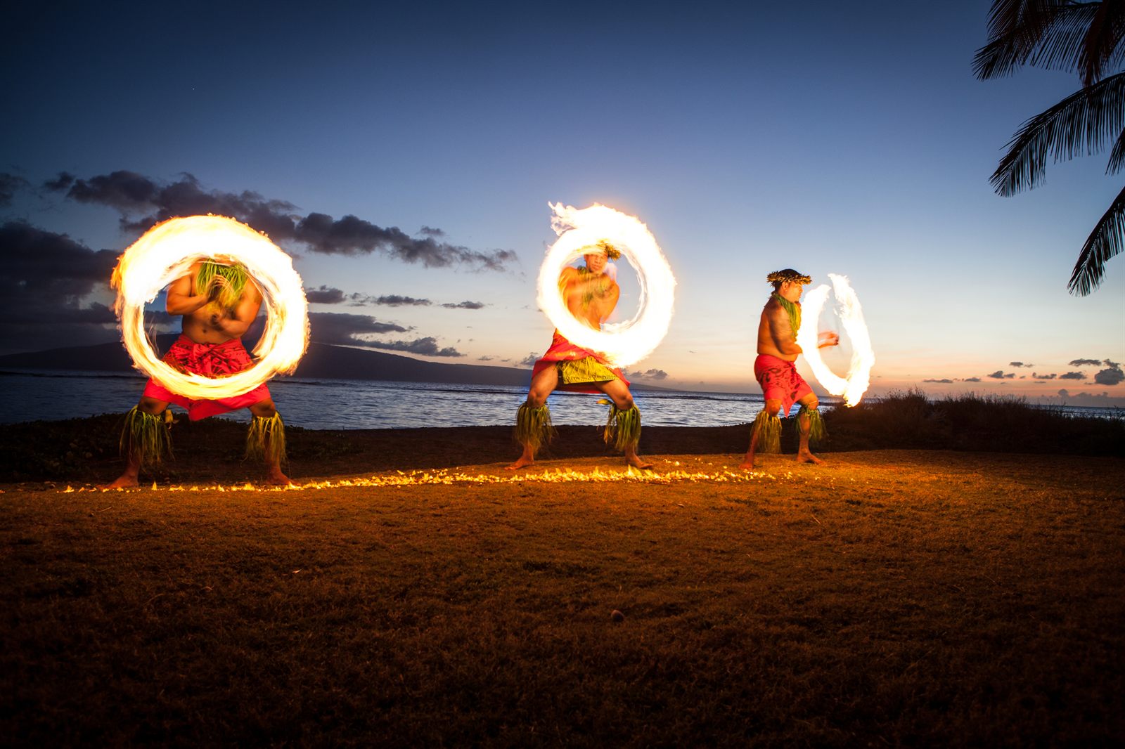 Fire dancers spinning flaming batons on a beach at dusk