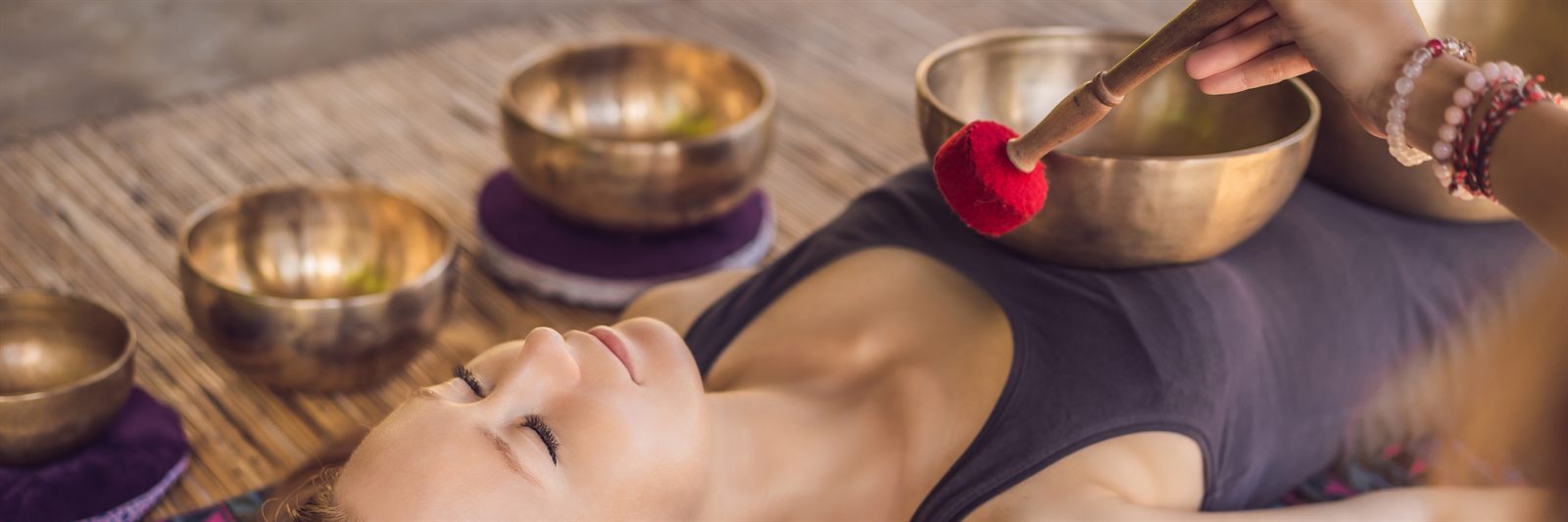 Woman relaxing on a massage table surrounded by brass singing bowls